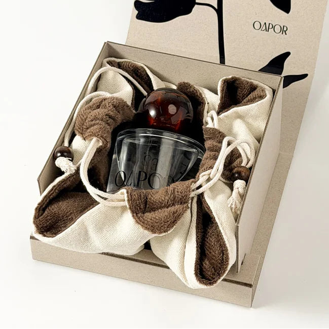 Gift set with a glass and brown fabric in a decorative box with floral design and 'Oapor' branding.